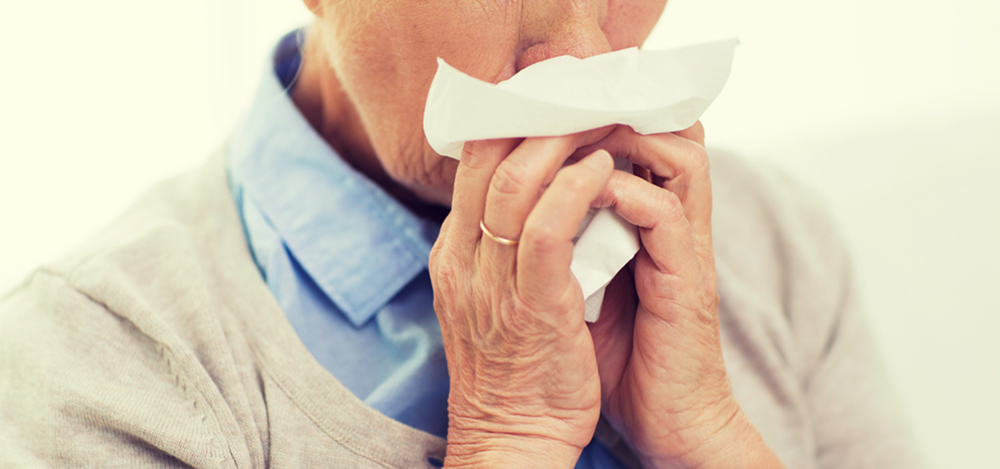 Elderly woman sneezing into a tissue.